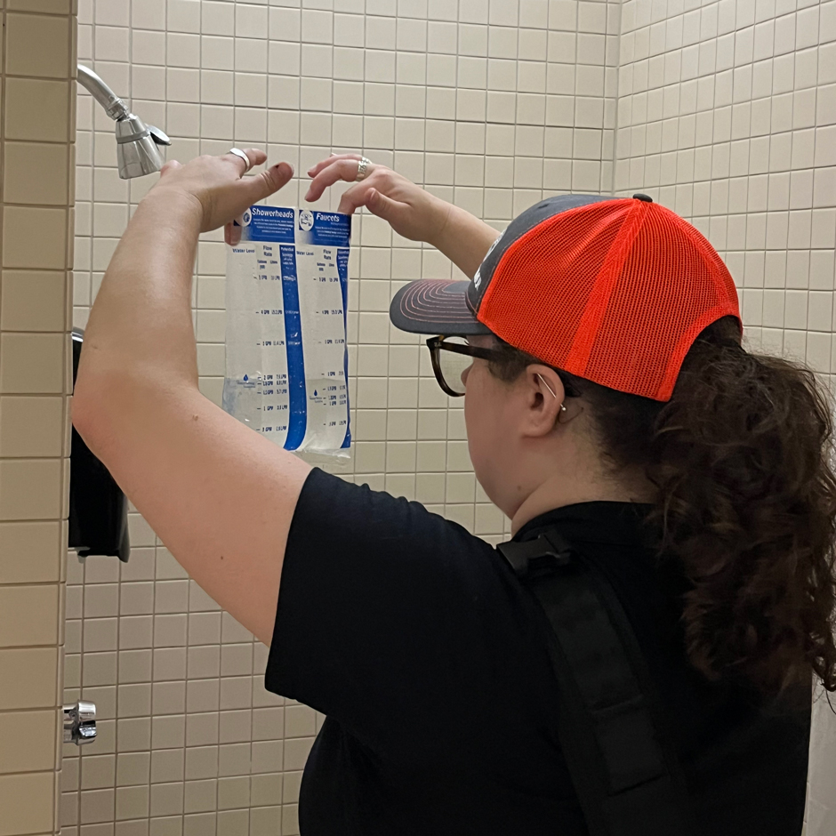 El miembro del equipo mide el flujo de agua en una ducha para determinar su uso promedio de agua.