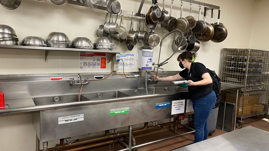 Team member inspects sink in a commercial-grade kitchen to check for leaks.