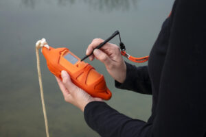 Environmental scientist, Katelyn Kubasky, holding the SonTek CastAway in front of the Fondriest Center for Environmental Studies field station pond