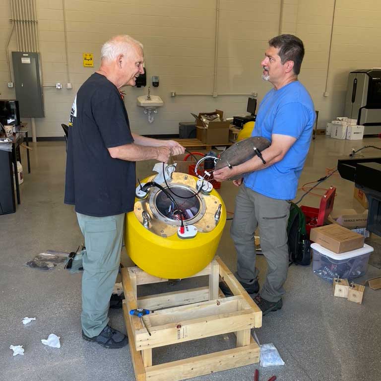 Buoy button-up is a breeze when working with long-time colleagues and friends – Dr. Val Klump (left) and Dr. Mike Zorn (right) discuss the system’s internal wiring configuration before sealing the data well with the custom-built stainless-steel lid. 